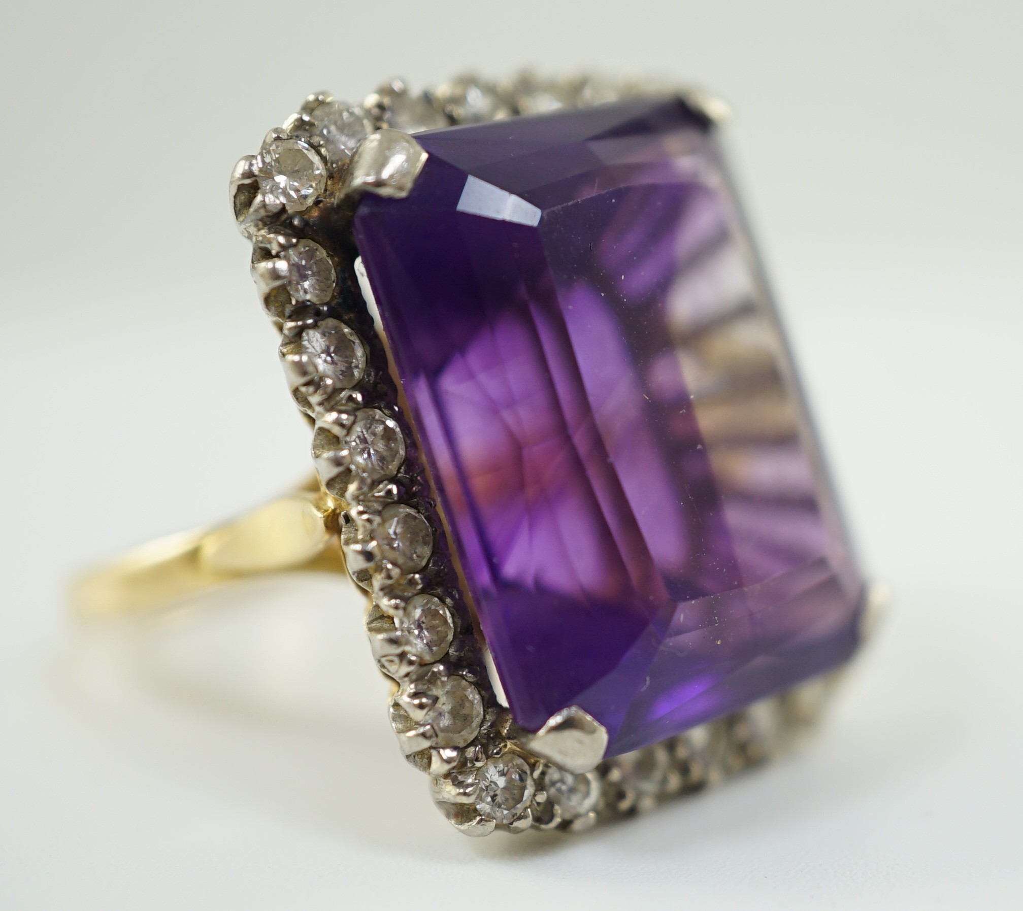 A large modern 18ct gold and emerald cut amethyst set dress ring, with diamond set border